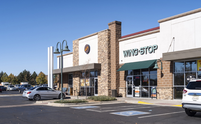 Parking lot and storefront of Wing Stop with trees behind it.