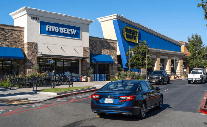 Car passing storefronts of Five Below and Best Buy.