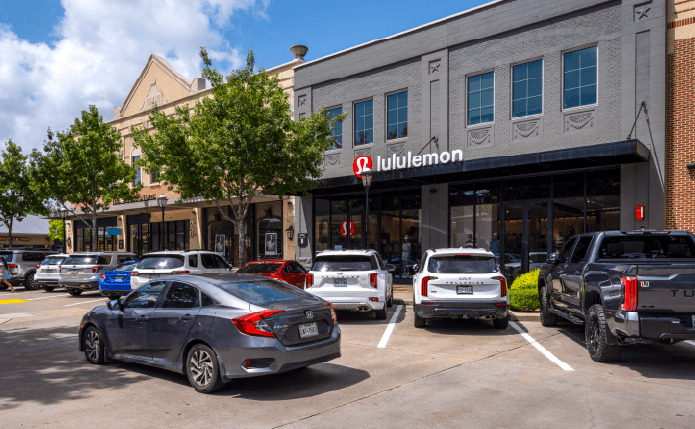 Busy parking lot in front of lululemon store with trees on left.