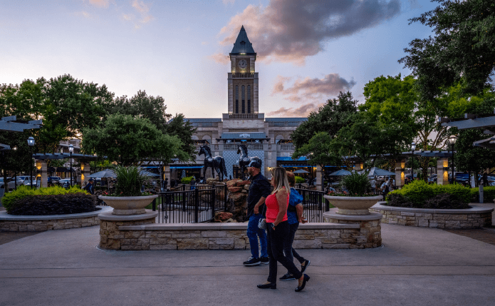 Group of patrons passes Clocktower and sculpture at shopping area.