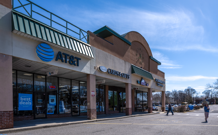 Pedestrians cross access road in front of shopping center stores like AT&T