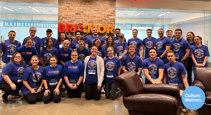 Group posing in office in front of brick column.