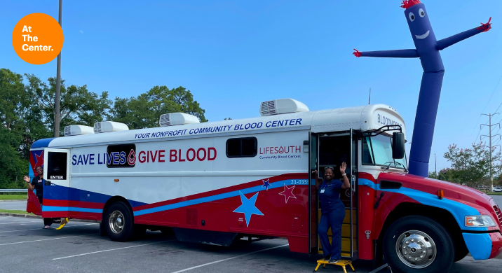 Truck for giving blood with woman waving in front door.
