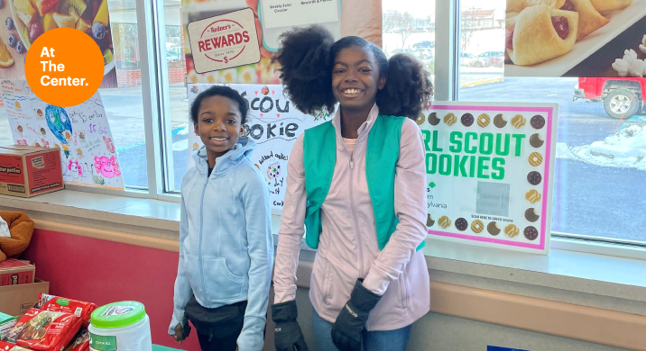 2 Girl scouts posing in front of table and cookies.