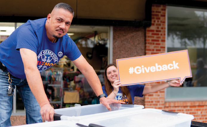 Male employee stacking boxes and female employee holding a #giveback sign