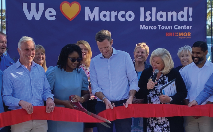 Employees cutting a ribbon with a "We Love Marco Island" banner behind them