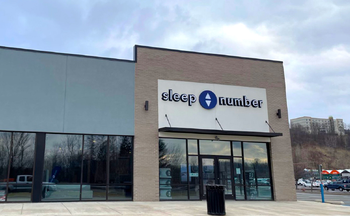 Sleep Number store with trash can in foreground and busy parking lot in the background.