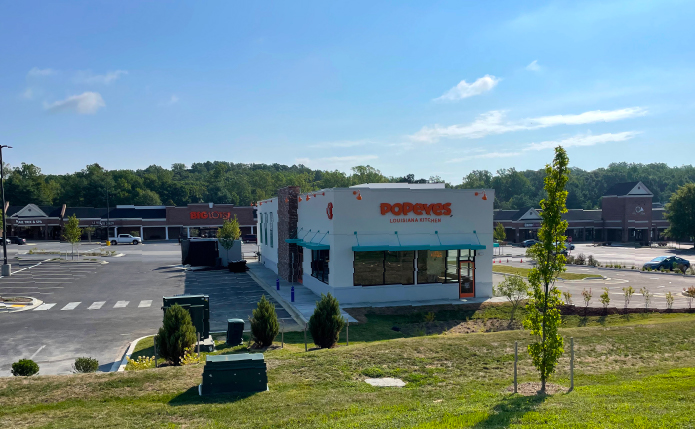 Popeyes outparcel store with parking lot and grass in foreground.