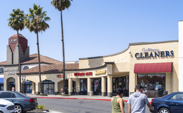 Shops and stores with palm trees on left and customers approaching in foreground.