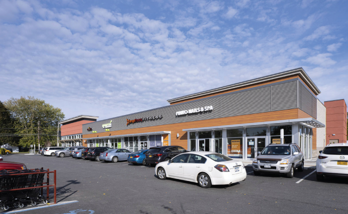 White car passing parked cars lining exterior of small shop space at Mamaroneck Centre in Mamaroneck, New York