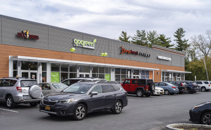 Dark grey hatchback driving past row of parked cars in front of small shop space at Mamaroneck Centre