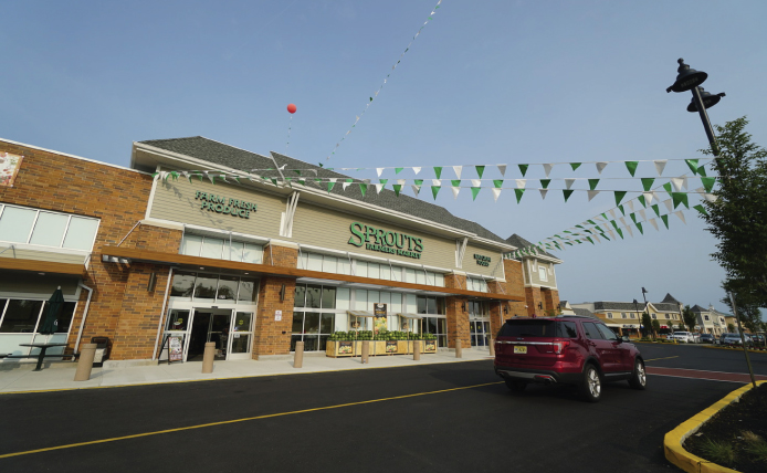 Green and white bunting hanging at Sprouts Farmers Market as dark red SUV passes at Marlton Crossing shopping center