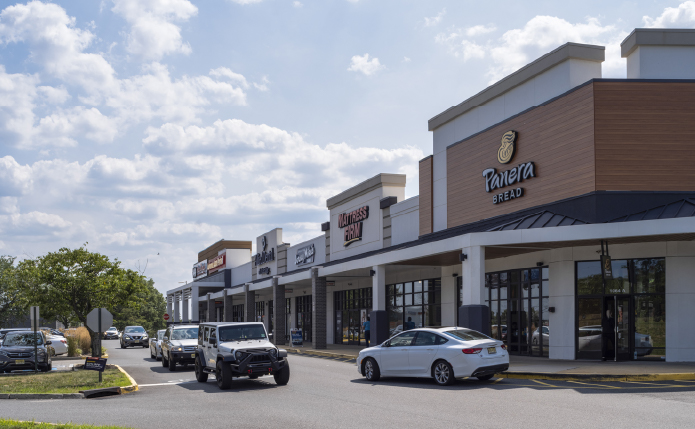 Cars passing Panera Bread on busy road.