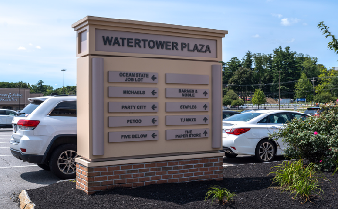 Pylon for WaterTower Plaza with cars behind it in parking lot.