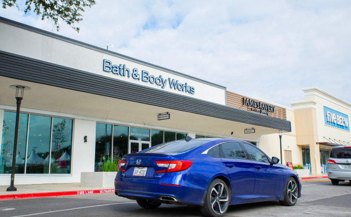 Blue car passing Bath & Body Works.