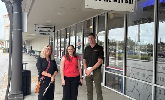 Three people standing outside retail storefronts, including Noire The Nail Bar, along a covered shopping center walkway.