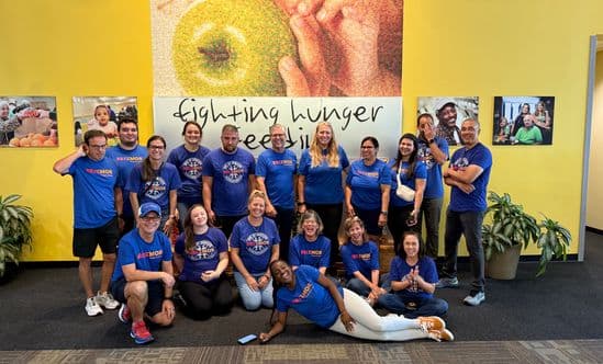 group of people in blue shirts posing in front of picture of an apple at a food bank