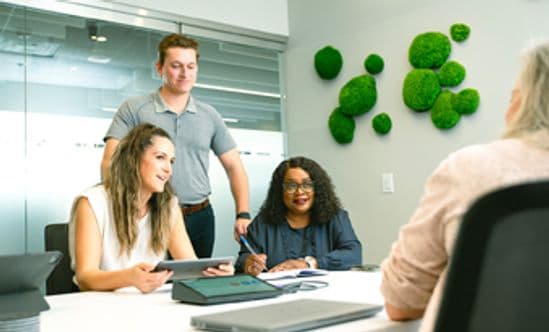 Two women and a man at a desk talking to somone off the right side of the image