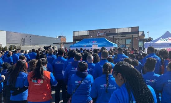 Crowd gathered in front of a Raising Cane’s with blue event tents during a community event.