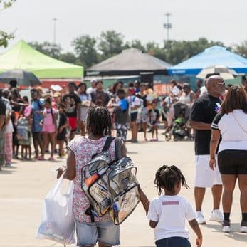 Woman and child in foreground walking towards tents in a parking lot event with lots of people
