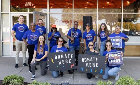 Group of employees holding Donate Here signs in front of a glass storefront