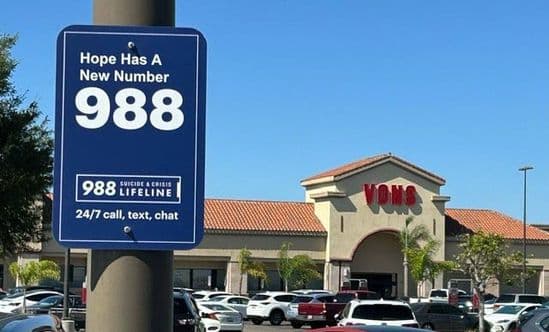 988 Lifeline sign for mental health crisis calls on a parking lot pole with Vons in the background