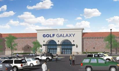 Rendering of Golf Galaxy at Westminster City Center in Westminster, CO, featuring a large modern entrance with arched storefront windows, decorative exterior lighting, brick façade detailing, landscaped walkways, and an active parking lot with multiple vehicles under a bright partly cloudy sky.