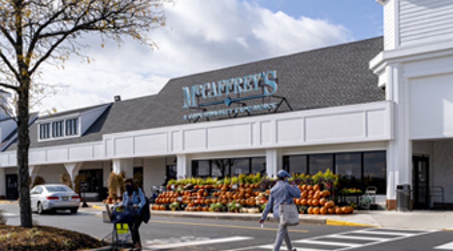 McCaffrey’s Food Market at Village at Newtown in Newtown, PA, shown with classic white clapboard architecture, teal signage, large covered walkway, and seasonal outdoor produce displays including pumpkins arranged along the storefront.