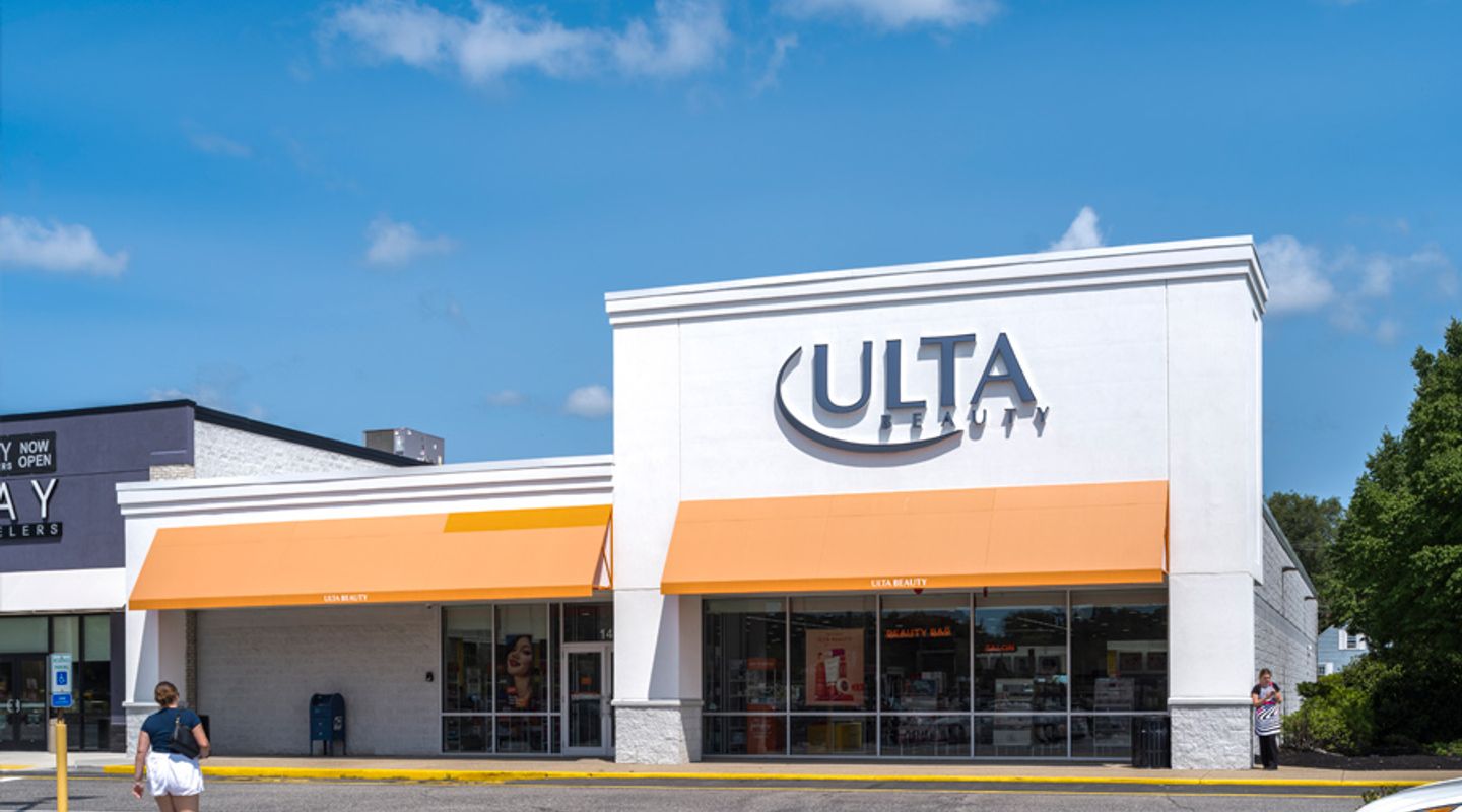 Ulta Beauty at Watertower Plaza in Leominster, MA, featuring a bright white façade with orange awnings, large storefront windows, accessible parking spaces, and a paved drive aisle under a sunny blue sky.