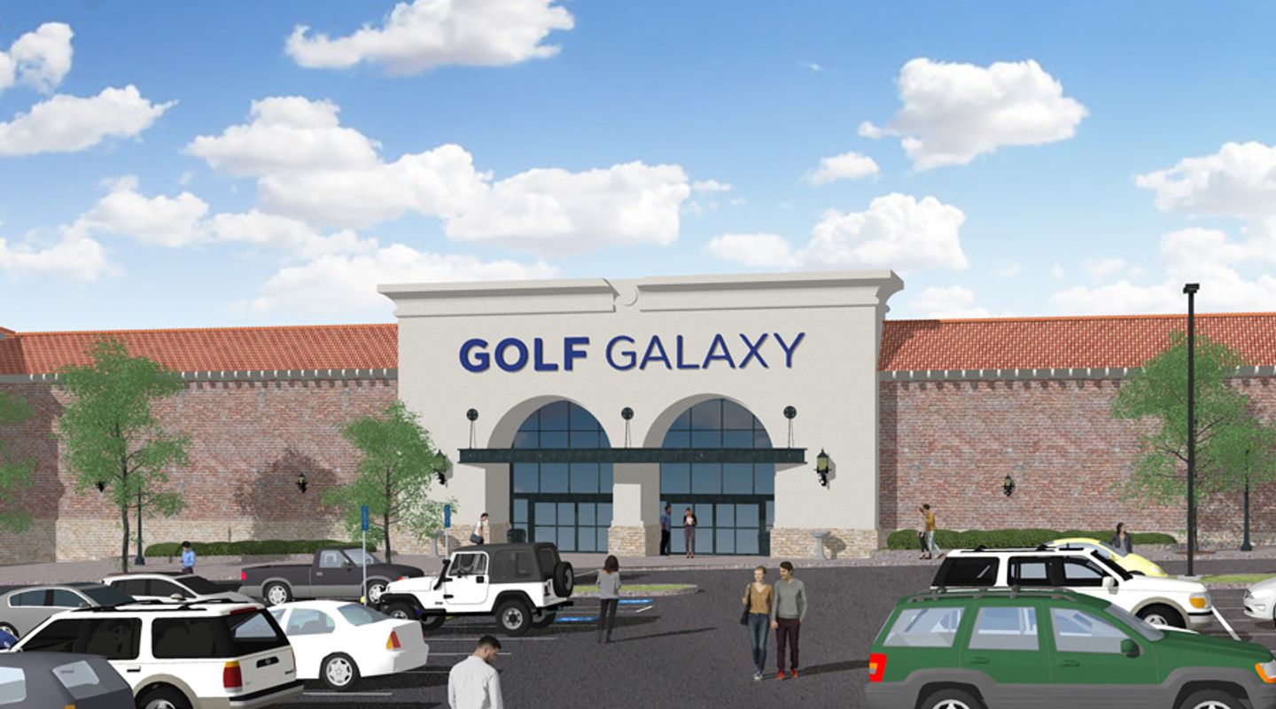 Rendering of Golf Galaxy at Westminster City Center in Westminster, CO, featuring a large modern entrance with arched storefront windows, decorative exterior lighting, brick façade detailing, landscaped walkways, and an active parking lot with multiple vehicles under a bright partly cloudy sky.