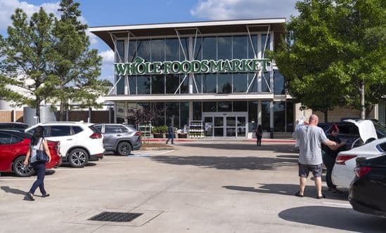 Whole Foods Market with trees on left and right sides of parking lot with shoppers and cars.